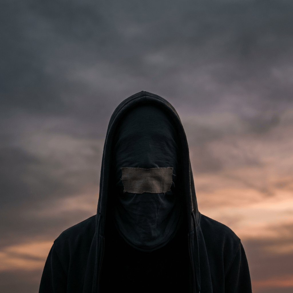 Person in a black hoodie with face covered and mouth taped shut at sunset.